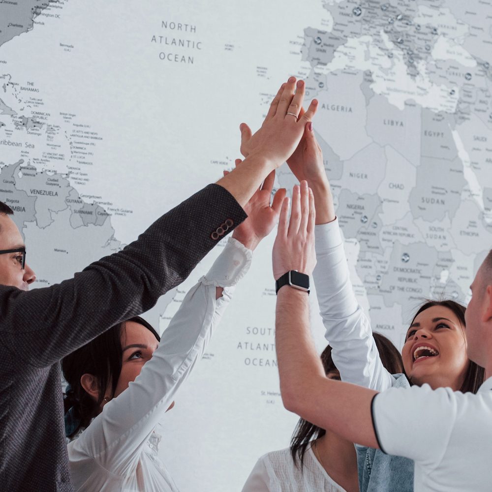 Celebrating success. Team of freelancers standing against wall with map of the world on it.