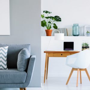 Patterned cushion on grey sofa in scandinavian home office interior with chair at desk. Real photo